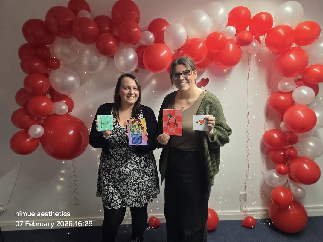 Two guests displaying their paintings beneath the red and white balloon arch at a Collective event.